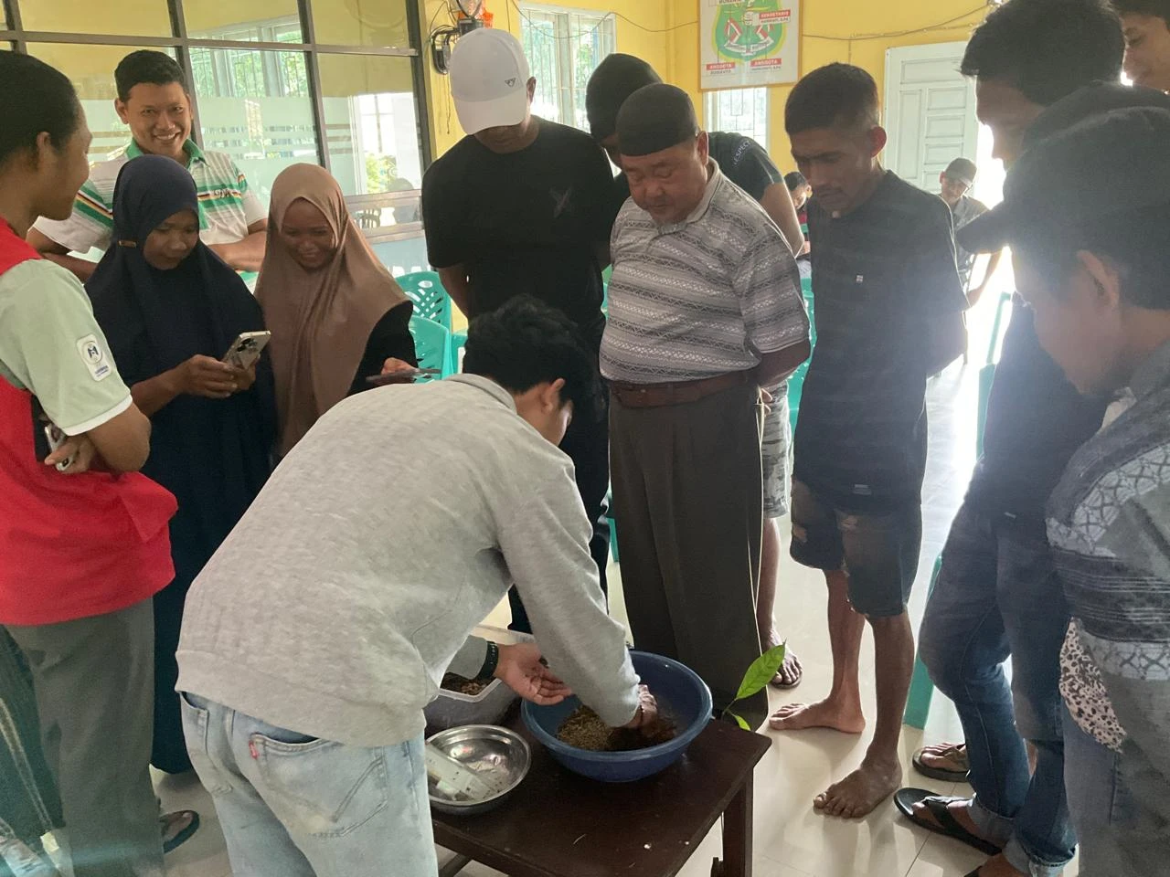 Warga Desa Anabannae mengerumuni meja praktik saat mahasiswa KKN Tematik 115 Universitas Hasanuddin mendemonstrasikan langsung proses budidaya maggot sebagai metode ilmiah pengolahan sampah organik menjadi pupuk alami dan pakan ternak bernilai ekonomi, dalam pelatihan lingkungan yang berlangsung interaktif di Kabupaten Sidenreng Rappang.